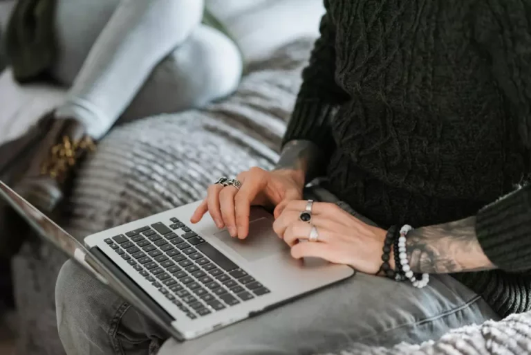 A woman named Katy, sitting on a bed, operates a laptop.