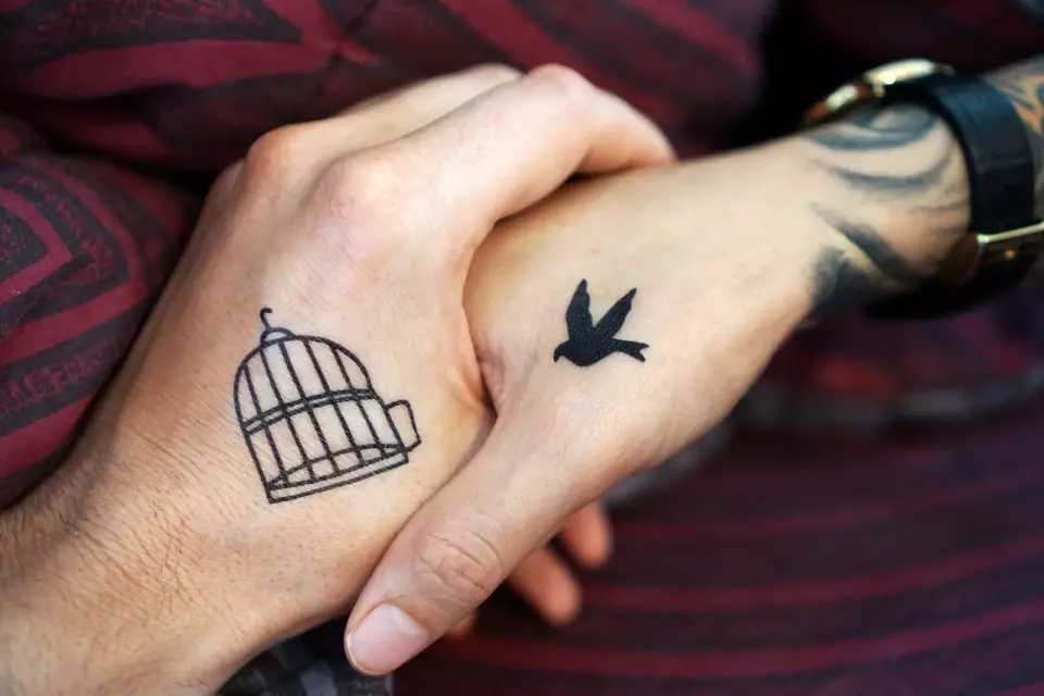 A couple with matching "bird cage" tattoos on their hands, symbolizing their unbreakable bond as best friends and soulmates.