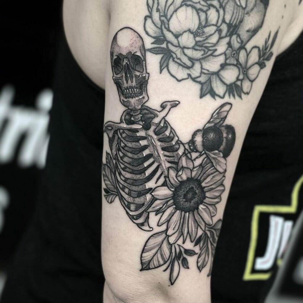 A black and grey tattoo of a skeleton and flowers by Katy.