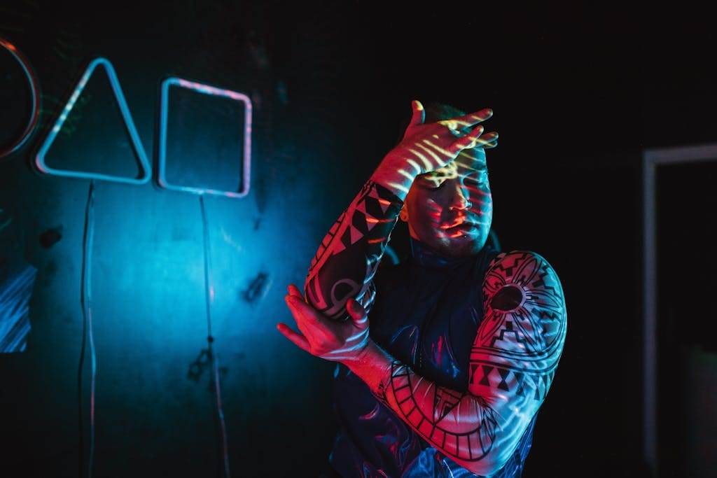 A man showcasing tattoos poses creatively under neon lights.