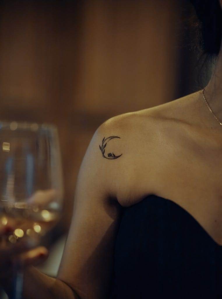 Close-up of a woman with a crescent tattoo holding a wine glass, showcasing elegance and style.