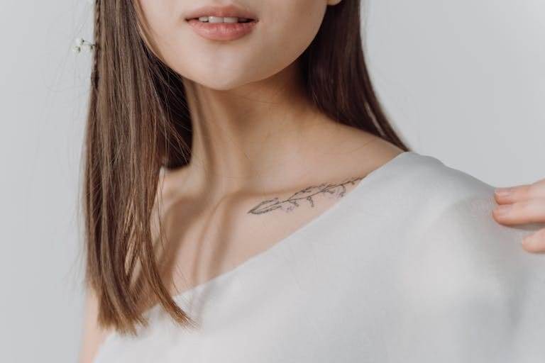 Elegant close-up of a woman's collarbone tattoo in a white top, highlighting subtle details.